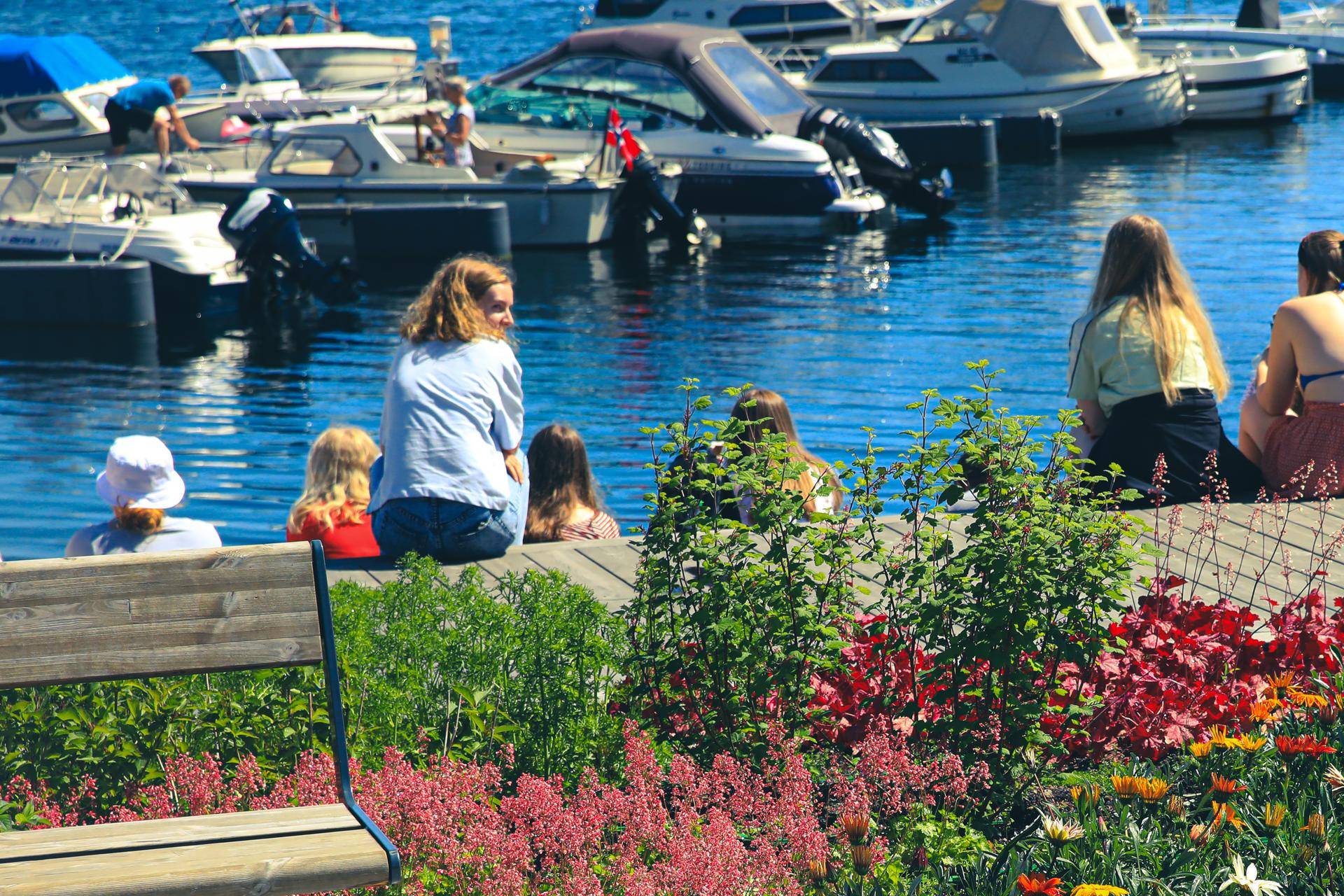 Mennesker som sitter på bryggekanten og ser utover båthavna