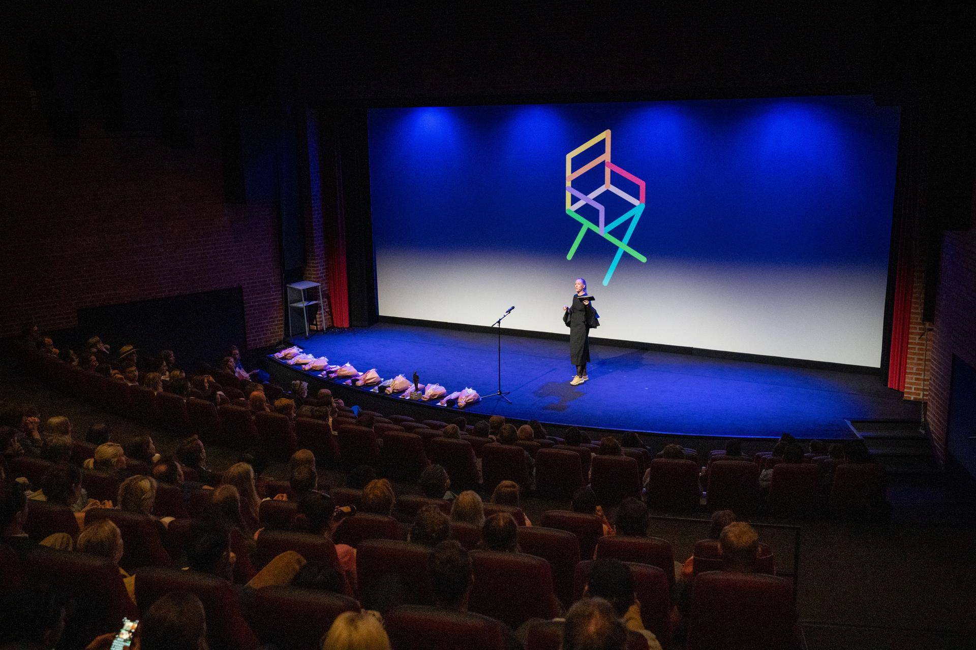 Kinosal, kvinne på scenen, fargerik logo på skjermen bak